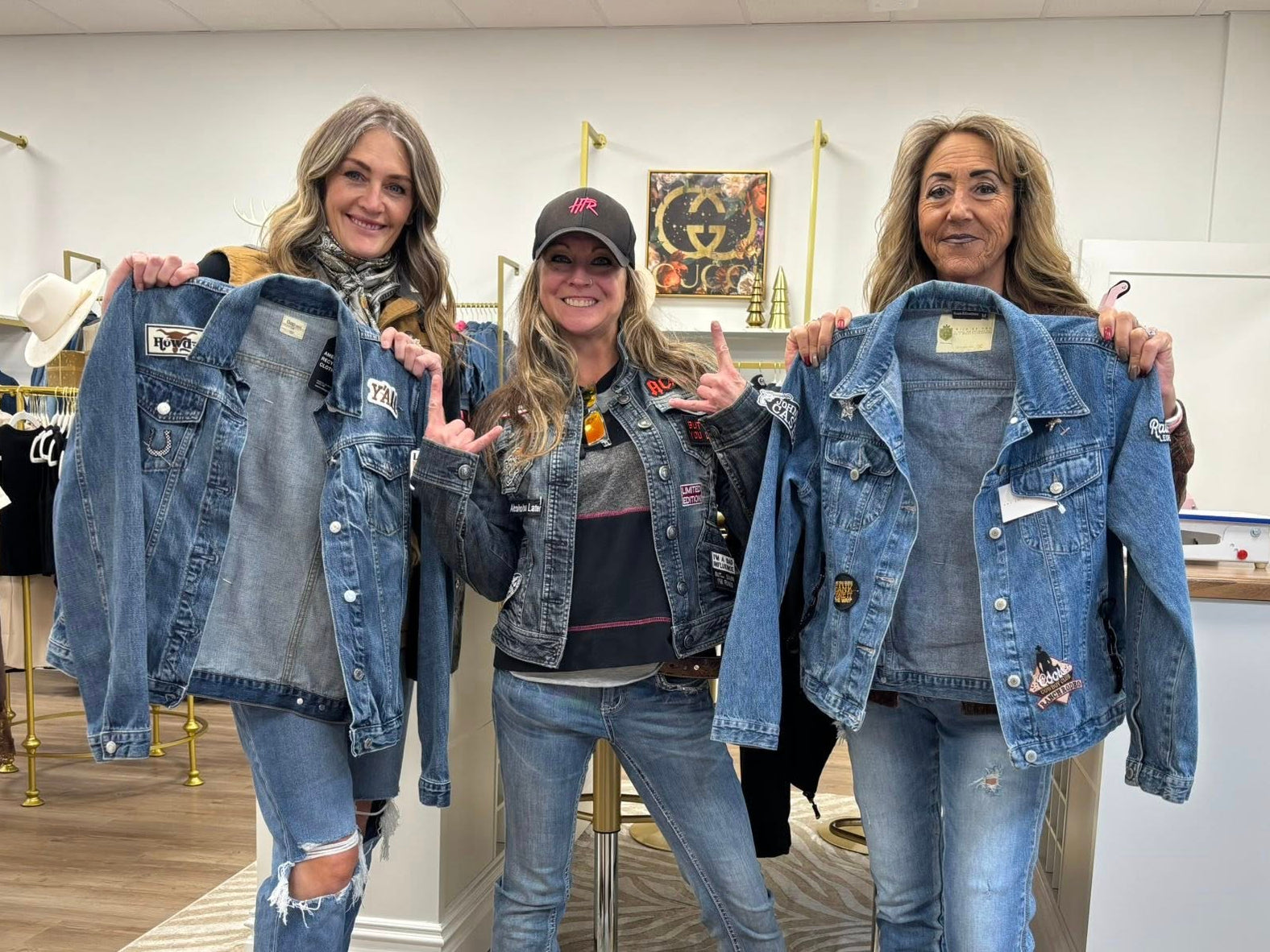 Three women in a store holding denim jackets and jeans

